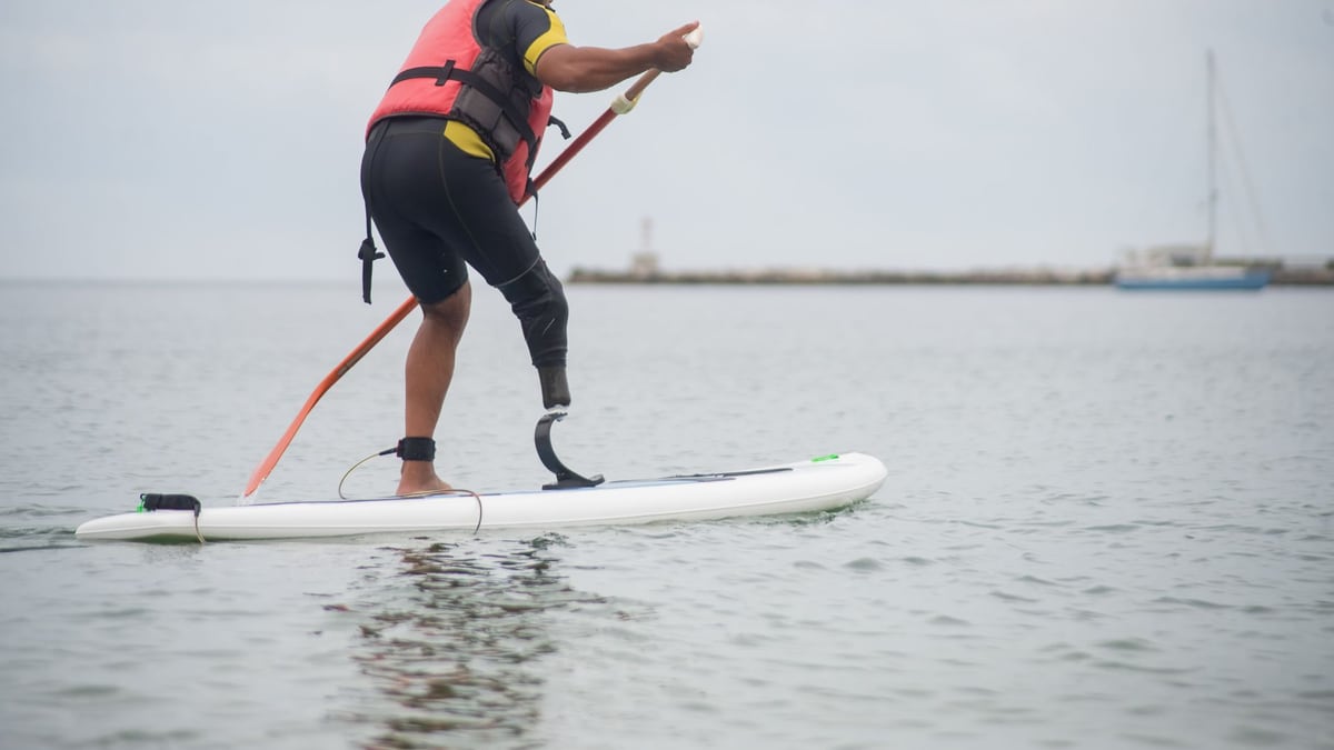 Man paddleboarding with prosthetic leg in Portugal, enjoying water sport.