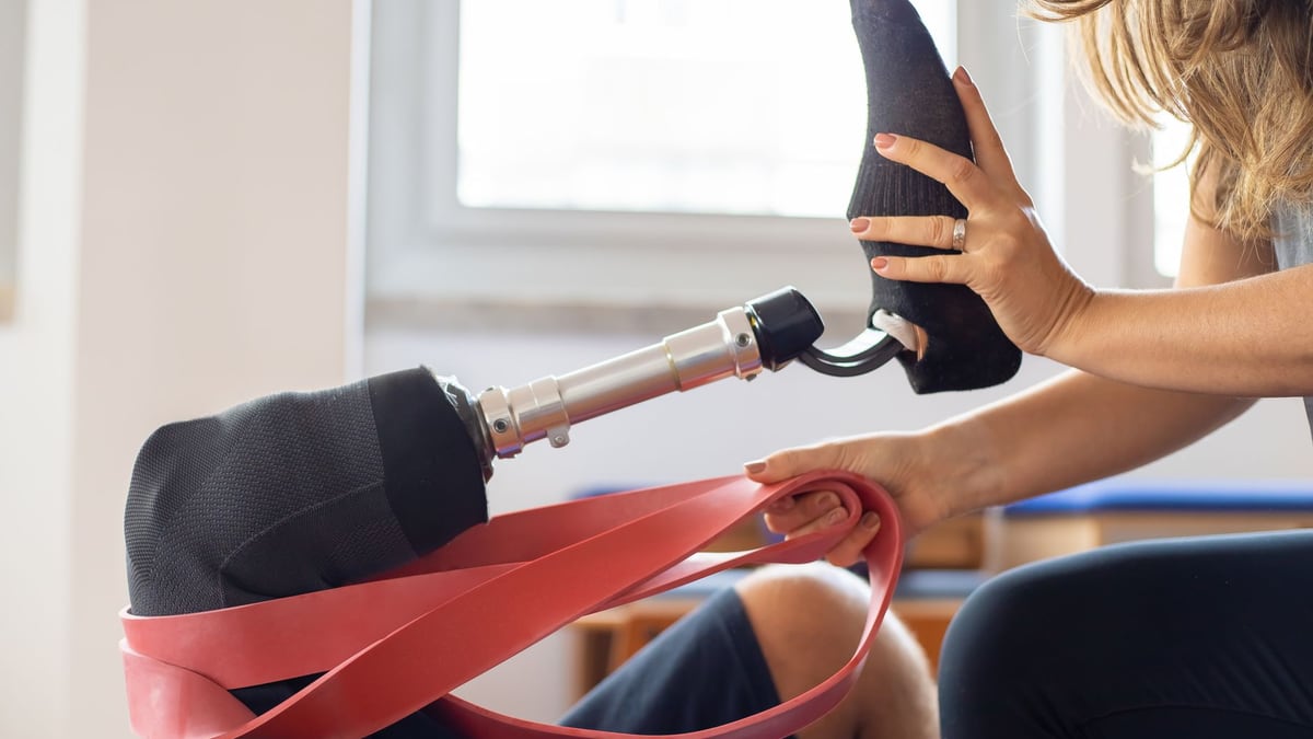 A close-up of a therapist assisting with prosthetic leg training indoors.