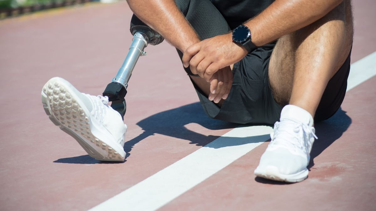 An athlete with a prosthetic leg sitting on a running track, wearing white sneakers.