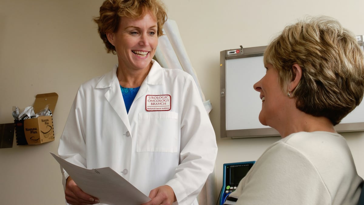 A smiling doctor in a white coat talking to a patient in a clinic