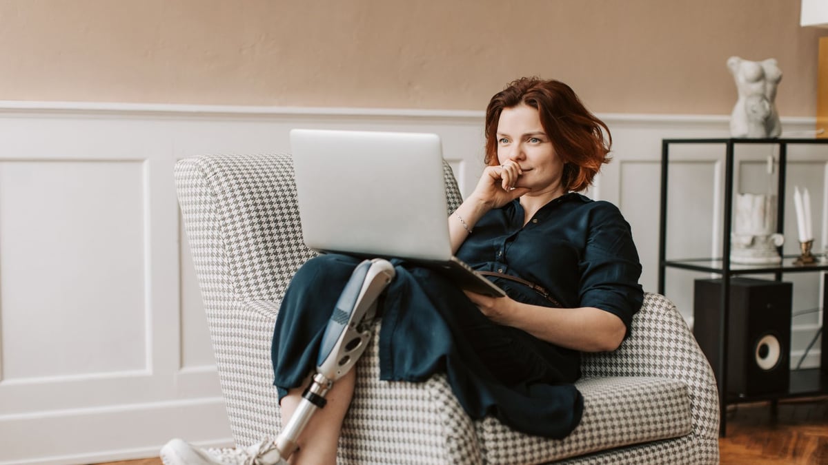 Woman with a prosthetic leg on a chair, working from home on a laptop.
