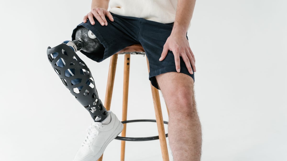 Adult male with prosthetic leg sitting on a wooden stool, wearing casual attire. Concept of disability and technology.