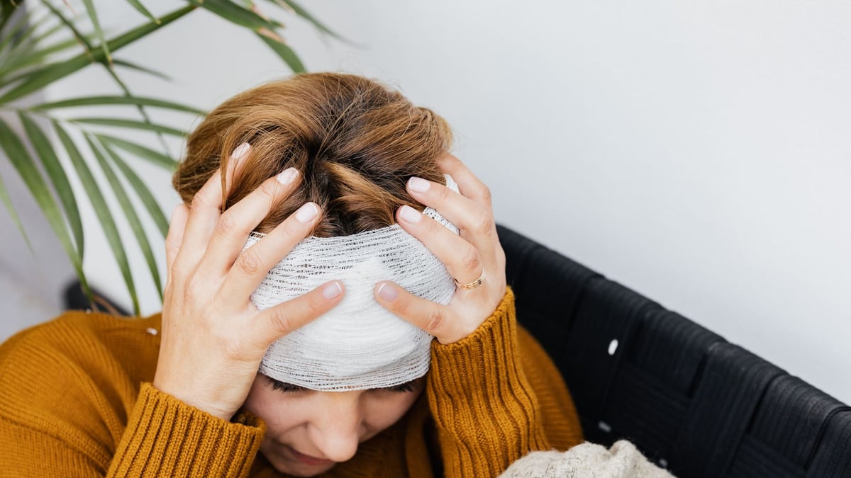 Woman with head injury holding her head in pain indoors.