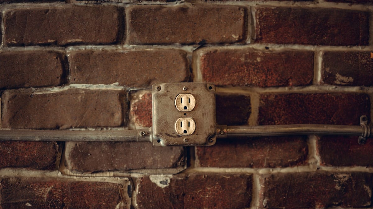 Rustic exposed brick wall featuring aged electrical sockets and metal conduit.