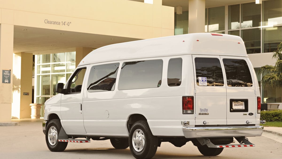 A large white passenger van parked in front of a modern office building entrance.